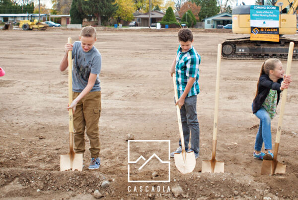 Five young kids with shovels standing on a large leveled dirt pad waiting to dig the first bit of dirt on a Cascadia of Boise's new construction site.