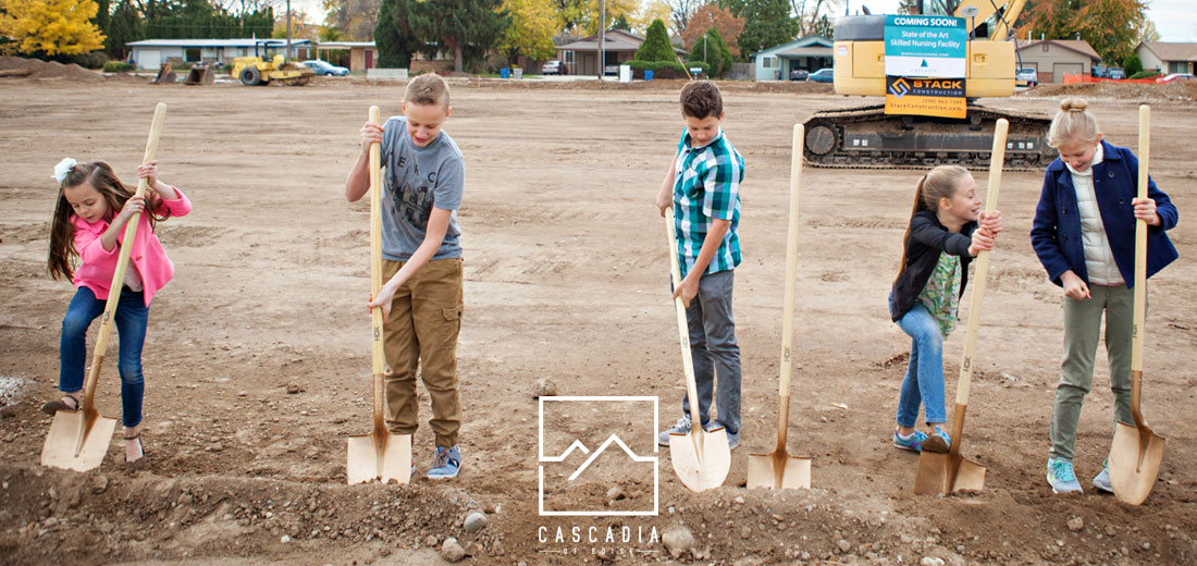 Five young kids with shovels standing on a large leveled dirt pad waiting to dig the first bit of dirt on a Cascadia of Boise's new construction site.