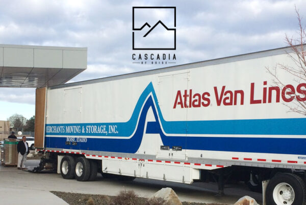 A large moving van is backed up under a portico entrance. Several people are standing at the back of the truck among boxes.