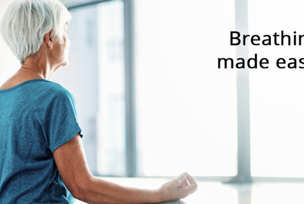 The back and side profile of a senior women standing and looking out a window while resting her arms on a deep window sill. The text "Breathing made easier" and the Cascadia of Boise logo are on the picture.